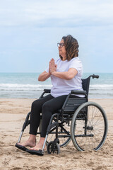 Mature woman in a wheelchair meditating at the beach