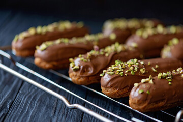 French dessert eclairs or profiteroles with milk chocolate glaze and pistachios. Pastry cakes with cream and topping. Soft selective focus.