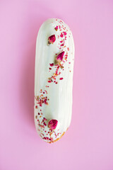 French dessert eclairs or profiteroles with rose-flavored white chocolate glaze, on a pink background. Pastry cakes with custard, rose cream and topping. Soft selective focus.