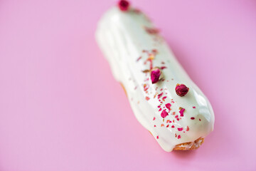 French dessert eclairs or profiteroles with rose-flavored white chocolate glaze, on a pink background. Pastry cakes with custard, rose cream and topping. Soft selective focus.