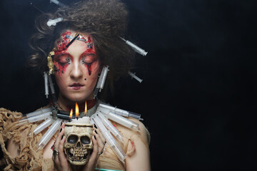 Young woman with creative makeup and hairstyle holding a candle in a skull candlestick