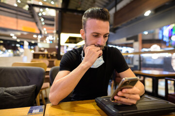 Man sitting at coffee shop while social distancing and using mobile phone