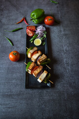 View from top of Paneer tikka in a black tray. Paneer or cottage cheese tikka is an Indian dish made out of chunks paneer marinated with spices along with vegetables and grilled in a tandoor. 