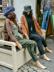 two mannequins (display dummy) sitting on a white bench in front of a store