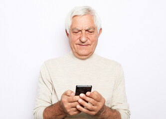 senior man in casual outfit using modern smartphone and laughing out loud while standing on white...