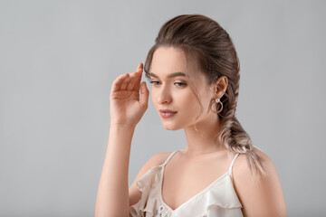 Beautiful young woman with braided hair on grey background