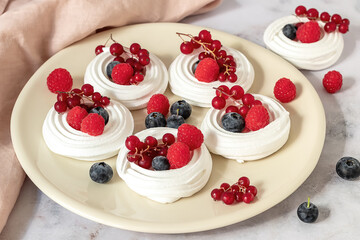 Fresh baking meringues or mini Pavlova on the plate. Sweet dessert decorated with different berries. 