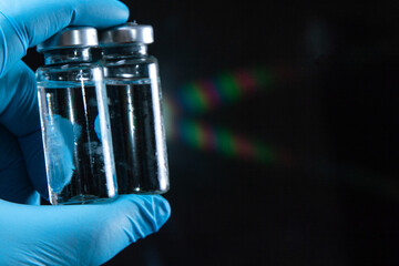 2 doses of Sars-Kov-2 coronavirus vaccine in transparent glass ampoules, covered with frost, on a dark background, short focus, toning