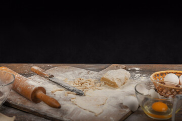 Women's hands, flour and dough. A woman in an apron cooking dough for homemade baking, a rustic home cozy atmosphere, a dark background with unusual lighting.