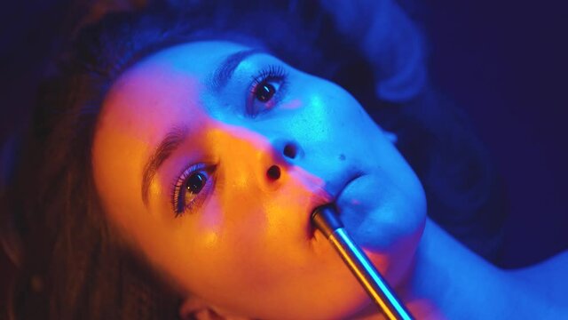 A girl smokes a hookah in a nightclub. Neon glow. Top view