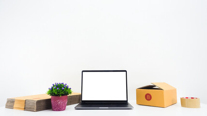 White notebook screen placed in the middle, next to it is a brown parcel box, adhesive tape, small tree with white background. Copy space concept. Online sales.