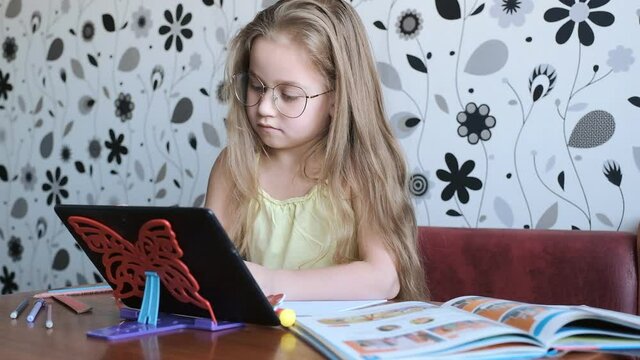 Distance learning. Home online learning. Little girl teaches English, speaks with a teacher online.