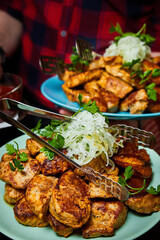 The waiter holds in his hands A plate with fried pork barbecue and onion. Close-up, selective focus.