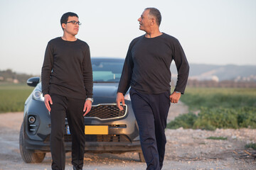 Teenager boy with father outdoors. Happy dad teaching teenage son to drive permission to drive, parenthood trust, family. Elderly father and young son standing next to car in nature on road trip.