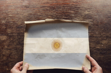 The white and blue national flag of Argentina on a torn piece of paper.