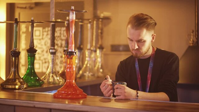 A hookah man hammers tobacco into a cone behind the bar. Working in the lounge bar