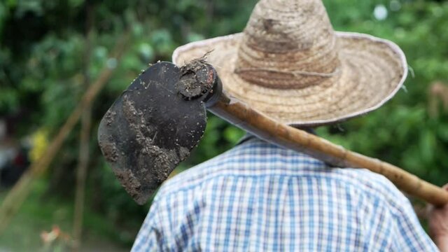 Old farmers in a straw hat held a hoe across his shoulder and facing the sky, waiting for the seasonal rain. Rural agriculture concept.