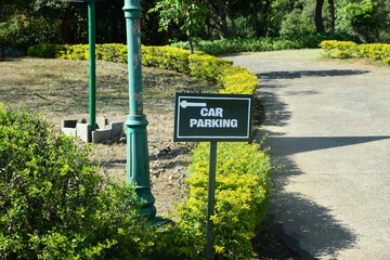 Car parking sign with arrow on green placard with shrubs and greens near the road.