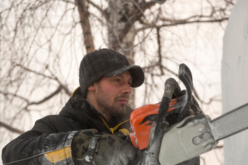 The sculptor cuts a figure from an ice block with a gasoline saw