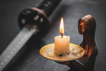 Katana sword and burning candle close up on the black table background with copy space.