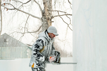 The sculptor cuts a figure from an ice block with a gasoline saw