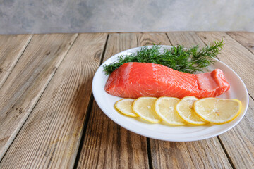 A piece of fresh trout fillet with lemon and dill greens on a white plate on a wooden table waiting for cooking. Restaurant menu. Dietary product. Keto diet. The concept of healthy eating.