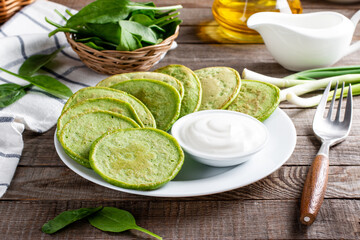 Green spinach pancakes with sour cream on a wooden table. Healthy food, diet
