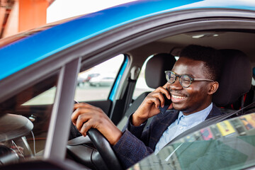 Man looking at mobile phone while driving. Portrait of a man using his cell phone while driving. Young man using his smartphone behind the wheel.