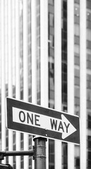 Obraz premium Black and white picture of a One Way traffic sign with blurred office building in background, selective focus, New York City, USA.