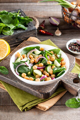 Green vegetable salad with chickpea, spinach, cucumber, red onions, and greens on a wooden table.