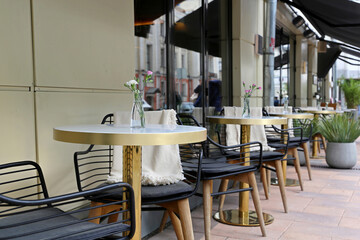 Street cafe with empty tables outdoor, city during coronavirus pandemic. Vases of flowers on a tables and vintage wooden chairs with warm plaids