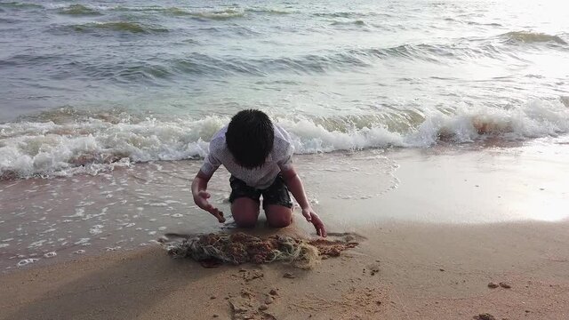 Asian boy is playing with fishing net rubbish on sand beach in Thailand.