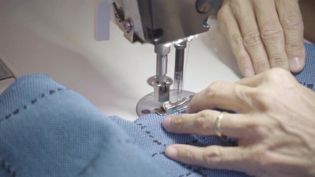 old woman hands sew blue cloth with sewing machine, slow motion textile detail