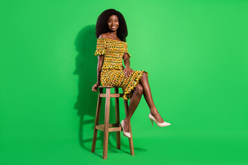 Full length photo of cheerful african woman happy positive smile sit stool isolated over green...