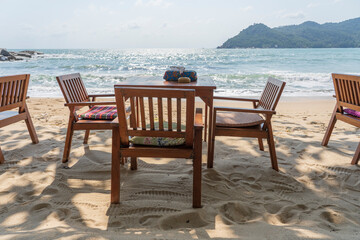 Wooden table and chairs in empty beach cafe next to sea water. Close up, Thailand