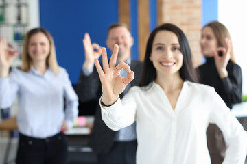 Businesswoman showing okay gesture on background of colleagues in office closeup
