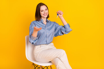 Photo of shiny charming young woman wear blue shirt smiling arm empty space holding keys isolated yellow color background