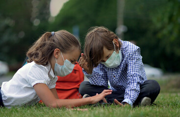 Cute pupils using smartphones at the elementary school. Boy and girl in safety masks with gadgets in their hands.