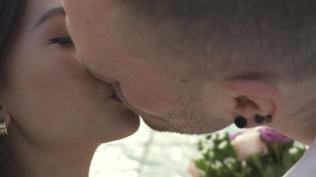 Happy groom with three-day stubble in men stud earrings kisses and hugs pretty bride sailing decorated yacht along sea extreme extreme closeup.