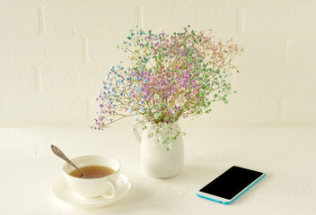Small colorful Gypsophila flowers on a white background. Soft home decor. flowers. blooming flowers in a vase.on a table with cup of tea and smartphone