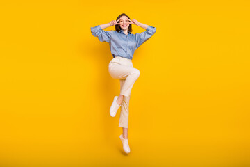 Fototapeta na wymiar Photo of adorable funny young lady dressed blue outfit jumping v-signs cover eyes smiling isolated yellow color background