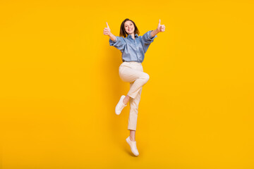Fototapeta na wymiar Photo of funky sweet young woman wear blue shirt smiling jumping high showing thumb up isolated yellow color background