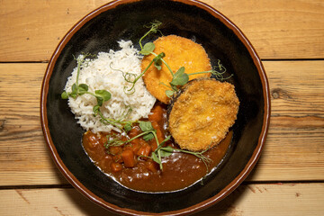 A delicious vegetarian meal of Aubergine Eggplant Katsu Curry with white fluffy rice on a wooden kitchen table