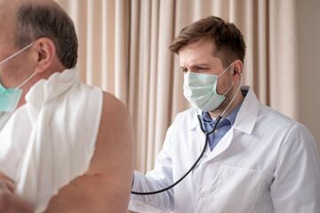 Caucaian male doctor listening to a senior male's breathing with a stethoscope