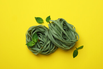 Uncooked green pasta and basil on yellow background