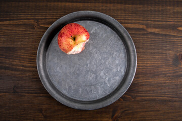 Bitten apple on a metal plate. Dark wood texture table