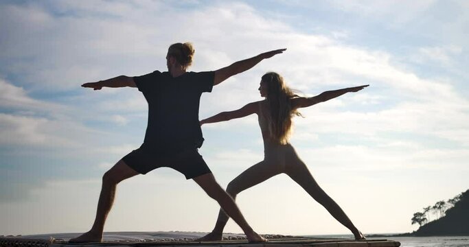 Silhouette of a caucasian man and woman with long hair finding inner peace by doing asana yoga exercises on beach at beautiful sunrise background. Healthy and Wellness lifestyle. Meditation concept.