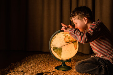 Boy studies the globe at night. The child sits on a mat on the floor.