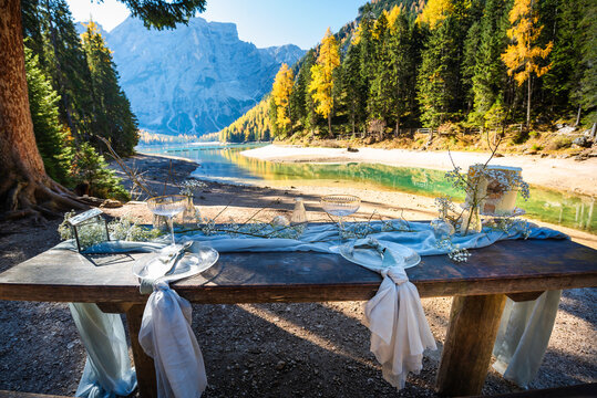 Set table for bride and groom on the background of a beautiful mountain lake. On the table are plates and other utensils, as well as cake. It's sunny autumn time.