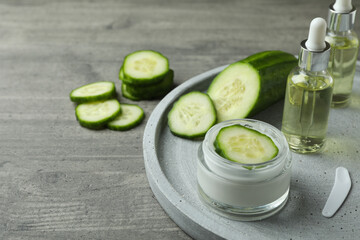 Cosmetics and cucumber on tray on gray textured background